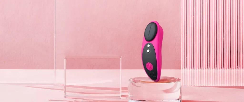 Dispositivo ergonómico de silicona médica rosa junto a su clip de fijación magnética.